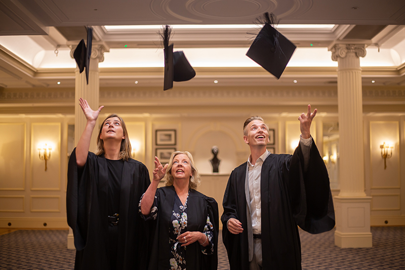 Three people throw mortar boards into the air