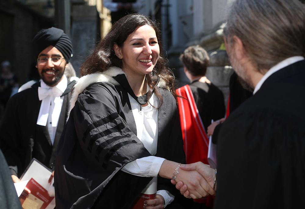 A student smiles and shakes hands with an academic on her graduation day
